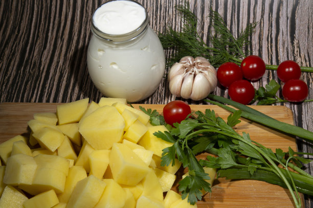 汤或烤肉的配料。切成片的生土豆放在切菜板上，旁边是蔬菜和酸奶油。烹饪概念图片下载