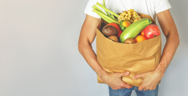 一个男人手里拿着一个装着蔬菜和水果的纸袋。图片下载