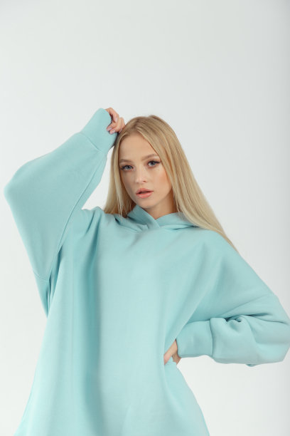 年轻漂亮的女人穿着蓝绿色的连帽衫和白色背景下的灰色自行车短裤图片下载