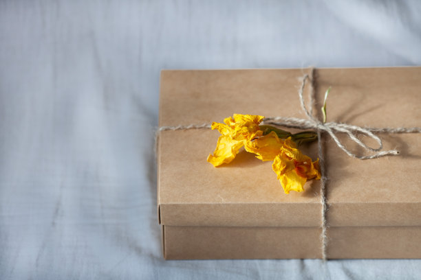 漂亮的礼品盒放在床上。简单的礼品包装，工艺盒，丝带缠绕，干黄色花朵，灰色亚麻织物背景。图片下载
