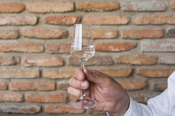 一个男人的手拿着装有格拉巴酒、伏特加和恰恰酒的玻璃杯。在一堵旧砖墙的背景上图片下载