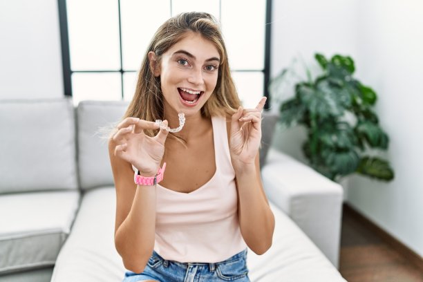 年轻的金发女人拿着隐形矫正器，脸上带着大大的微笑，用手指指着一边看着摄像机。图片下载