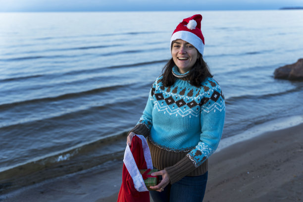 一个戴着圣诞帽的快乐年轻女人从袋子里拿出圣诞礼物图片下载