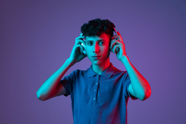 小男孩穿着t恤，戴着耳机在霓虹灯下的紫色背景下听音乐图片下载
