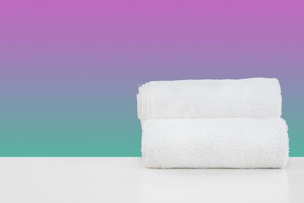 将干净的毛巾叠放在白色的桌子上，以颜色为背景图片下载