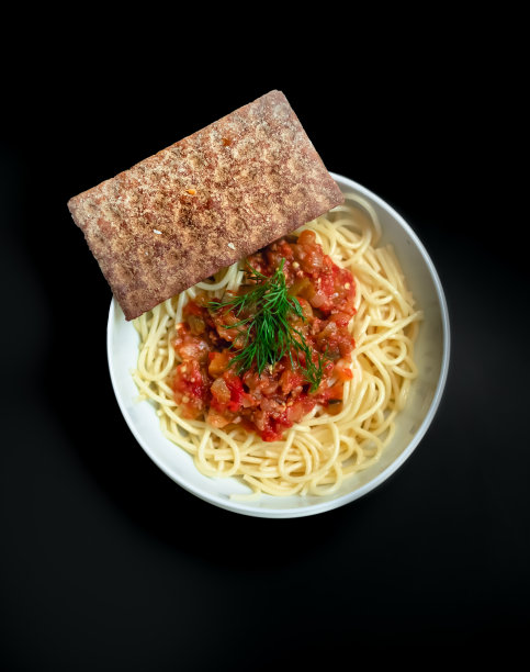 圆形碗里有番茄酱面食和黑色背景的饼干，俯视图图片下载