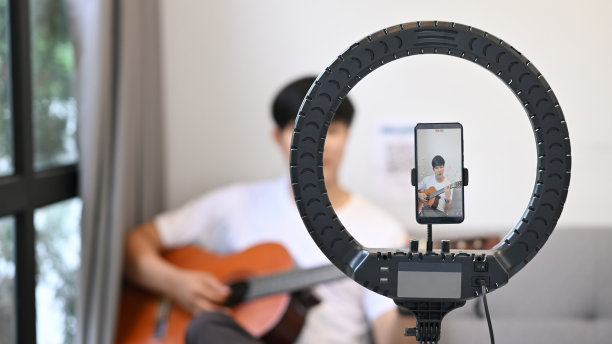 年轻的亚洲人在家里用智能手机弹吉他和在线视频博客。图片下载