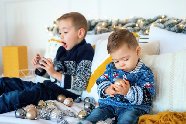 专注于可爱的小婴儿检查他手中的圣诞玩具。哥哥在后面鬼混。圣诞节或新年的心情。可爱的家庭在家里玩得很开心图片下载