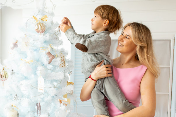 一张幸福家庭的照片，妈妈和儿子装饰圣诞树。蓝白相间的新年圣诞装饰。家庭圣诞快乐的概念。图片下载