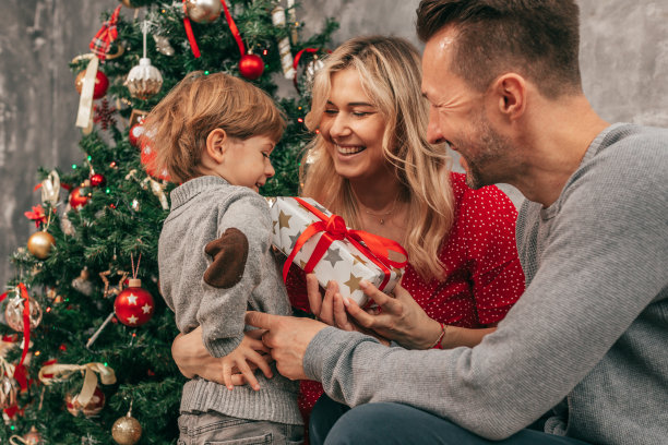 爸爸、妈妈和儿子的照片。花时间在一起。家里有圣诞树，幸福时刻。为假期做准备。快乐的在一起。玩礼品盒。红绿颜色。新年前夕图片下载