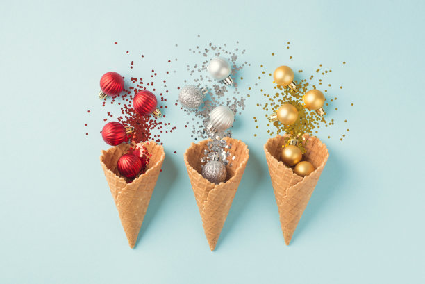 俯视图照片的三个冰淇淋甜筒与圣诞装饰爆炸的红色银色和金色的圣诞树球和亮片在孤立的淡蓝色背景图片下载