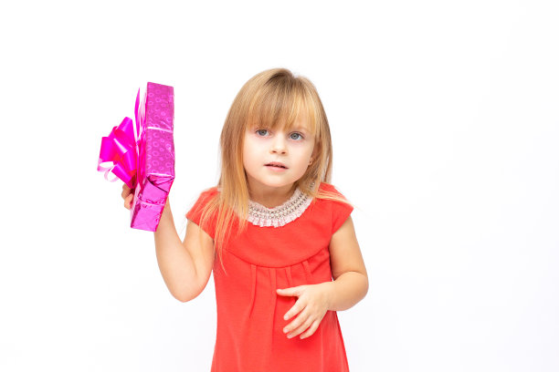 快乐的小女孩穿着红色的裙子，拿着粉红色的礼物盒，隔着白色的背景横幅复制空间图片下载