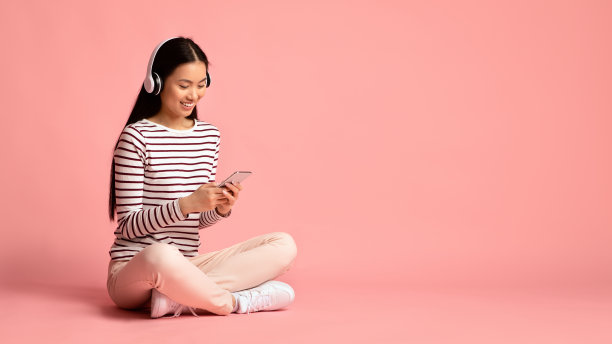 最喜欢的休闲。快乐亚洲女士听音乐与智能手机和无线耳机图片下载