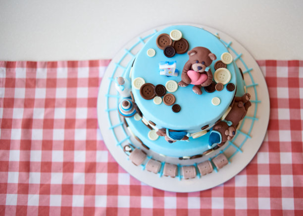 圆形多层蓝色生日蛋糕，上面装饰着纽扣、玩具、小熊、火车头和一号，放在格子台布上，为文本复制空间。俯视图图片下载