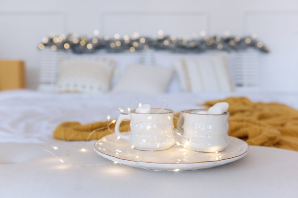 白色的陶瓷托盘上，两杯香甜的棉花糖，五彩缤纷的花环在床上。节日的内部图片下载