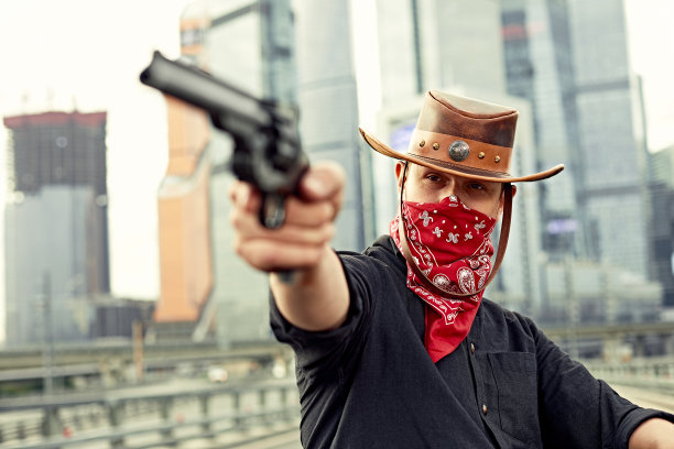 一名穿着黑色皮夹克、戴着头巾的时髦男子的肖像，他坐在定制的复古摩托车上，看着远处，背景是大城市的建筑图片下载