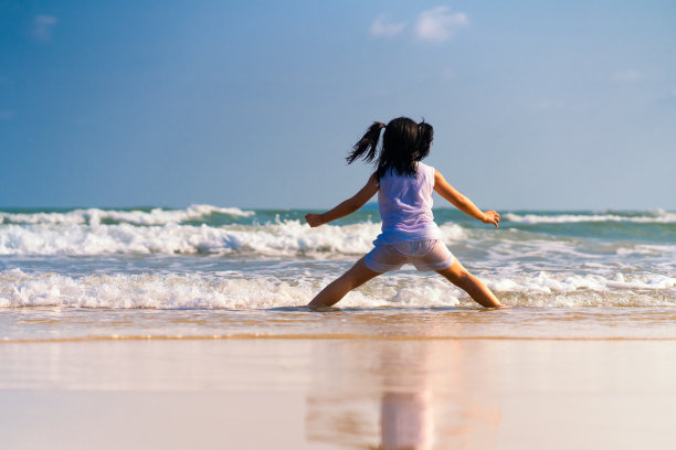 一个穿着白色连衣裙的女孩在风和阳光中快乐地在海里玩耍，这让女孩感到一种宁静的气氛，适合在美丽的海边度假图片下载