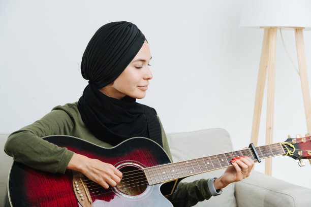年轻的穆斯林妇女戴着宗教头巾弹吉他图片下载
