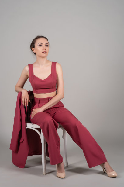 全身照片吸引别致的商务女士坐在椅子上，穿着红色西装，高跟鞋孤立的灰色背景图片下载