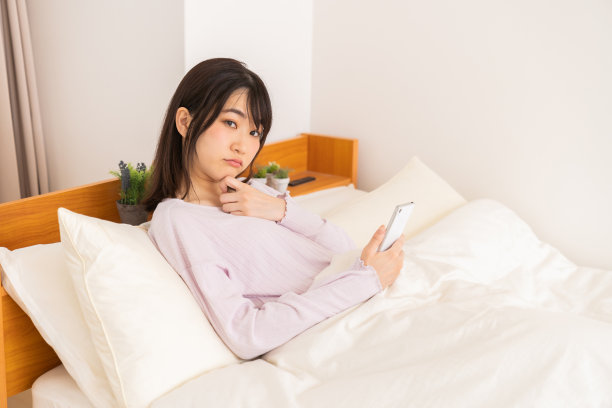 漂亮的亚洲女人在床上用智能手机，想想图片下载