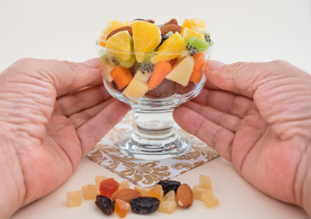 男性手拿着一个盛满新鲜和五颜六色的水果沙拉的玻璃碗。苹果，猕猴桃，橘子，木瓜，芒果，甜瓜。早餐或休息，健康饮食。图片下载