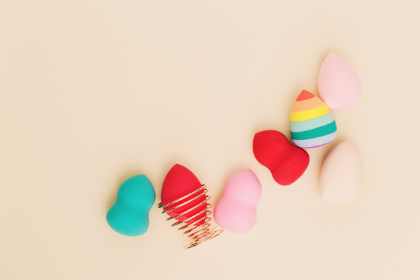 彩色化妆品美容海绵接近不同形式的米色背景与复制空间。俯视图，平躺。图片下载