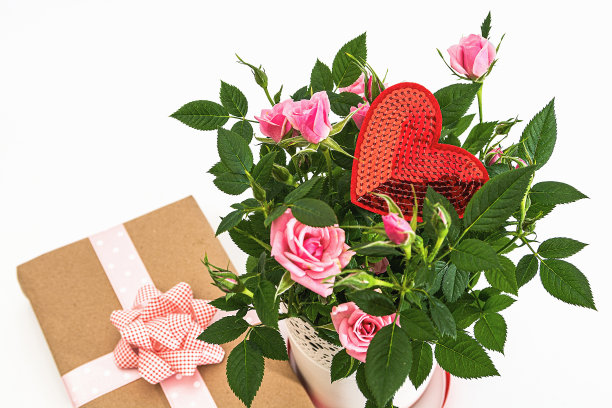 白色花瓶内的玫瑰花束，白色背景上的情人节卡片和礼物包装纸。从上面的观点图片下载