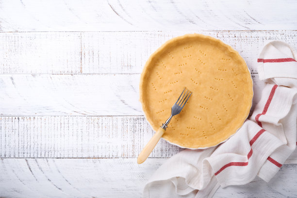 生面团用于烤蛋饼，馅饼或派在陶瓷烤制形式准备烤在厨房毛巾上在白色旧乡村木板木制背景。俯视图，复制空间。假日自制烘焙的概念。图片下载