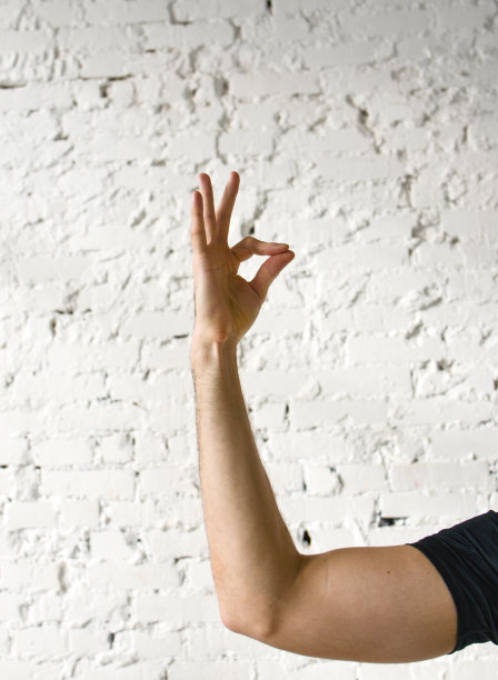 瑜伽的一个手势。一只手靠在白色砖墙上。图片下载