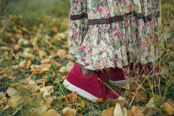 女腿穿着红色运动鞋和长裙，背景是秋叶和草地图片下载