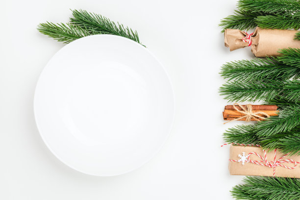 顶视图特写在白色空盘子与复制空间在白色孤立的背景与框架的圣诞装饰杉木树枝，礼品盒和肉桂图片下载