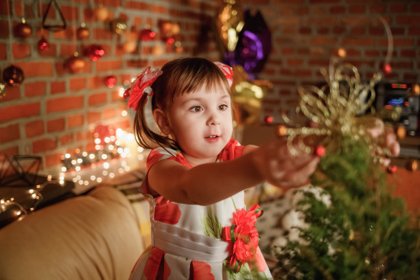 圣诞节的孩子的照片。可爱的小女孩的肖像旁边装饰的圣诞树。新年回家派对快乐图片下载