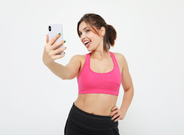一名带着智能手机的微笑健身女性的肖像。有问题的时间。在白色背景图片下载