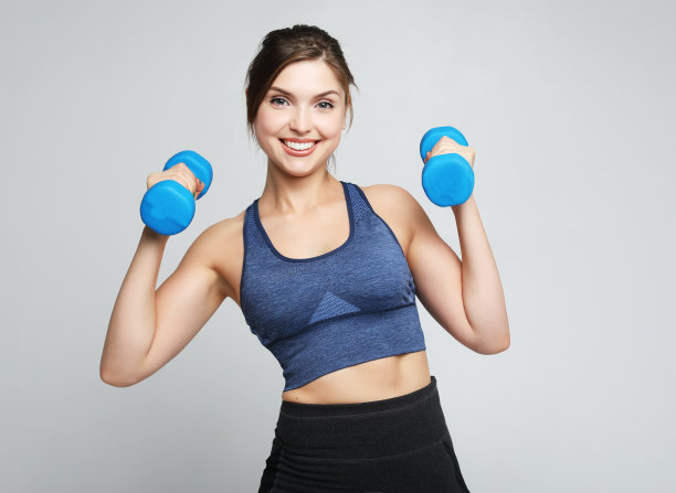 一张健康健康的年轻女子微笑着把哑铃举在肩上的照片。运动与人的概念图片下载