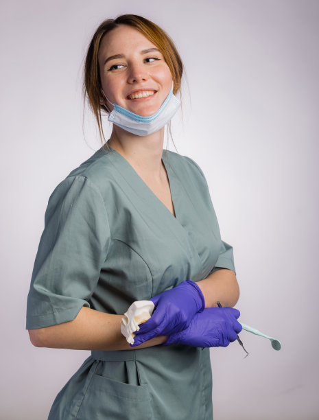 照片中的女牙医带着工作工具，戴着统一的医用口罩和乳胶医用手套。灰色背景下，手持塑料义齿、牙齿和工具图片下载