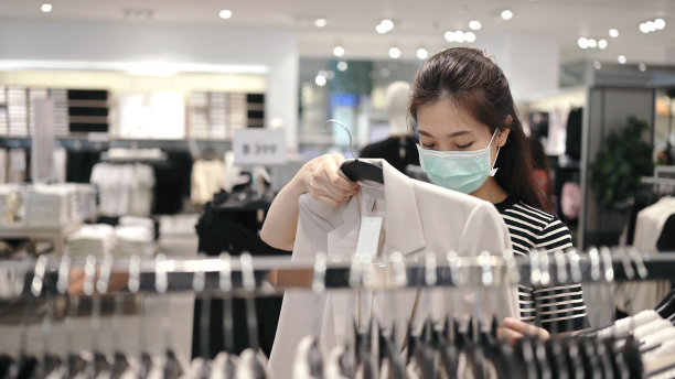 新常态下的快乐购物：戴防护口罩的年轻亚洲女性在下班后在城市服装店试穿衣服图片下载