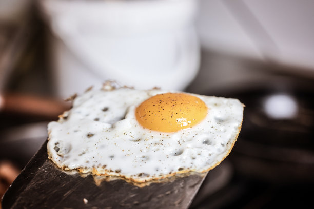 一个煎蛋，撒上黑胡椒末，放在金属铲上图片下载