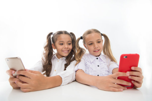 在学校写博客。在智能手机上写博客的快乐小女孩。小女孩们回到学校。科技让生活更轻松图片下载