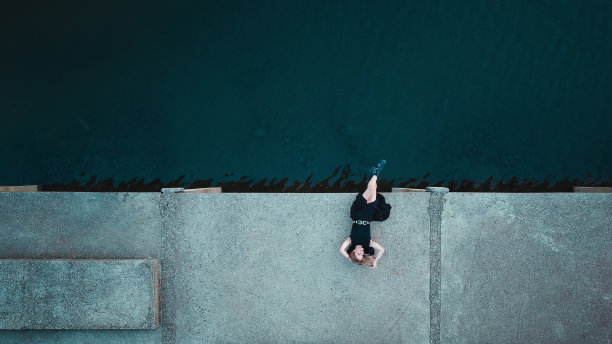 一个美丽的年轻女子站在水泥湖码头上，无人机从上面拍摄图片下载
