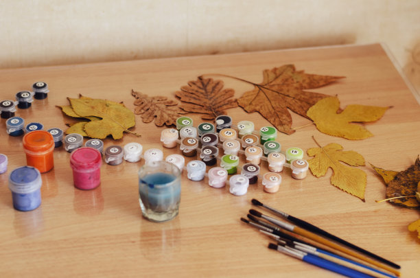 干树叶，一套颜料和画笔在桌子上作画。图片下载