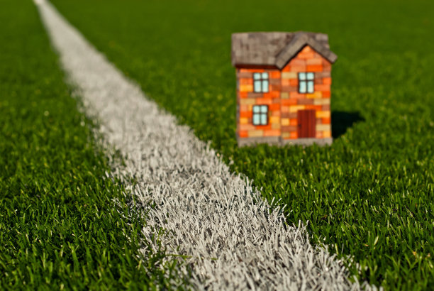 草地上的砖玩具房子。绿色草地上的橘黄色房子。自己的住房和建筑的概念。草地上的白色条纹模仿道路。图片下载