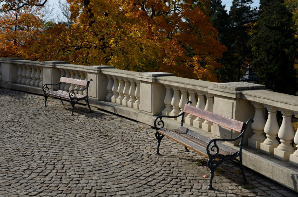 栏杆旁的城堡在秋日的阳光下，枫叶泛黄。木制的长凳上。带有海洋主题波浪的金属分隔柱和系柱。不受马车轮子的伤害图片下载