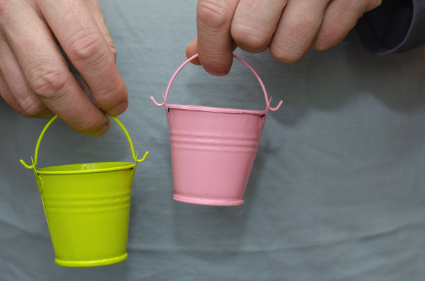 两个男人的手拿着玩具桶。粉红色和绿色的婴儿桶图片下载