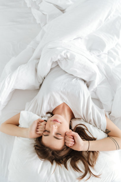 漂亮女人躺在家里的床上伸懒腰。图片下载