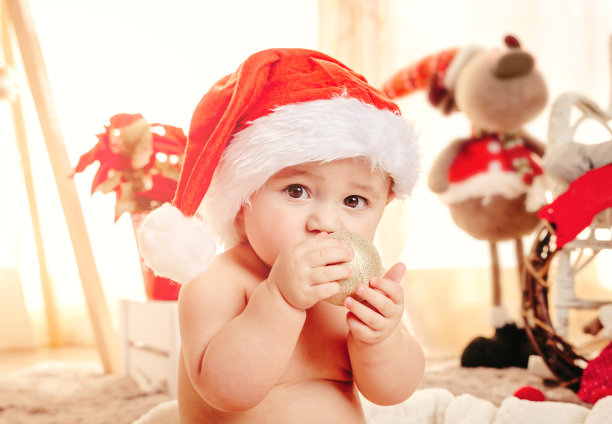 戴着圣诞帽和装饰品的可爱圣诞宝宝。舒适的毯子上玩耍的小孩。圣诞快乐和冬季节日概念。图片下载