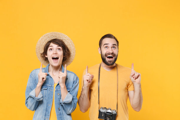 兴奋的游客夫妇朋友男孩女孩夏装帽子与照片相机孤立在黄色背景。周末出国旅游的乘客。空中飞行的旅程。伸出食指。图片下载