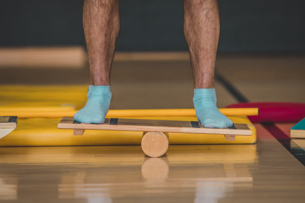 男教练使用木质平衡板的正面照片。在室内体育馆可以看到不同的平衡运动器材。图片下载