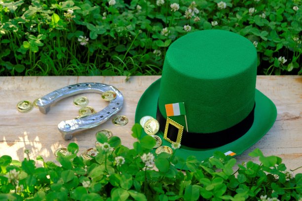 St.Patrick的一天。绿色的小妖精帽子，爱尔兰的旗帜，金色的装饰硬币，在绿色三叶草木制背景上的马蹄铁。爱尔兰传统的春假。图片下载