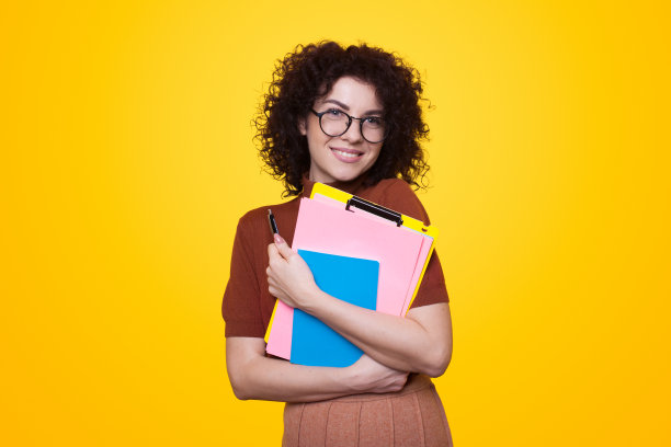 一头卷发的学生拿着黄色背景的文件夹。为教育设计的时尚肖像。图片下载