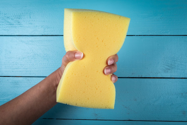 黄色洗涤或绘画海绵在妇女的手在木制背景图片下载